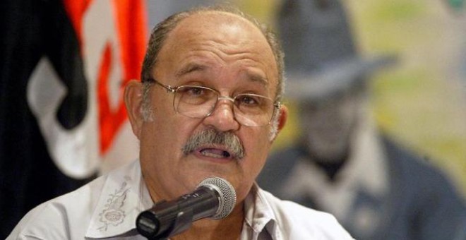 Miguel D'Escoto, ofreciendo una charla delante de la bandera del Frente Sandinista de Liberación Nacional y la imagen del líder nicaragüense Augusto Sandino.