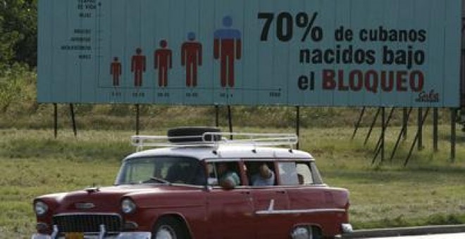 Un coche pasa en La Habana junto a un cartel que recuerda que el 70% de cubanos ha nacido bajo el bloqueo. -