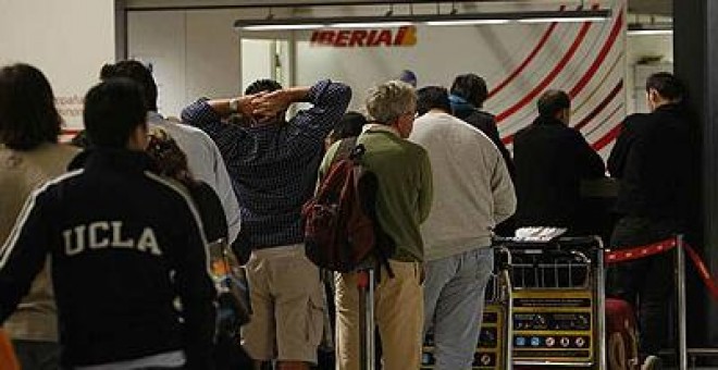 Pasajeros hacen cola frente a un mostrado de Iberia en la T4 de Barajas.