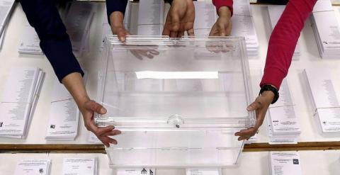 Tres personas sujetan una urna sobre las papeletas en un colegio electoral. EFE