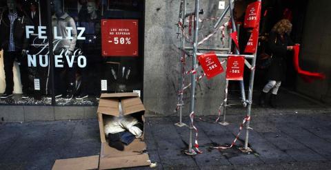 Una mujer sale de una tienda en rebajas mientras un hombre duerme en unas cajas en la calle en Madrid. REUTERS