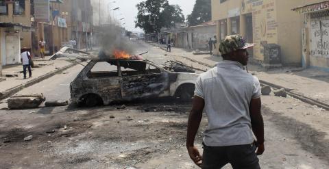 Un hombre junto a un coche quemado en Kinshasa a modo de barricada. - REUTERS