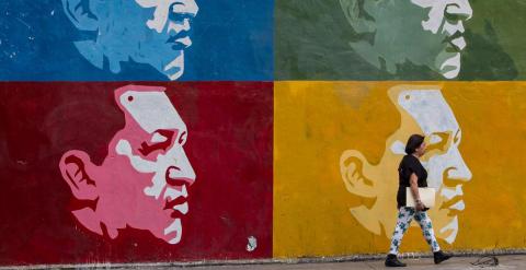 Una mujer camina frente a un muro con imágenes de Chávez en Caracas. - EFE