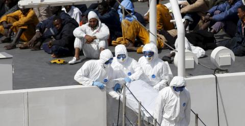 Agentes sacan del barco el cuerpo de un inmigrante muerto ante la mirada de los supervivientes en el puerto de La Valleta. /REUTERS