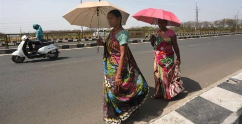 Mujeres indias caminan por la carretera con unos paraguas tapándose del sol. /EFE