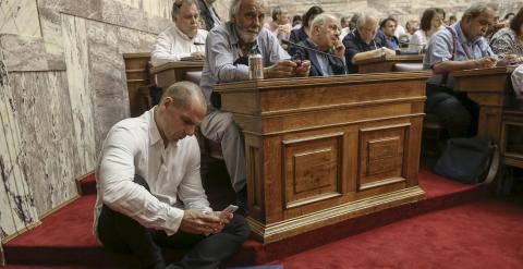 El ministro griego de Finanzas, Yanis Varoufakis consulta su móvil sentado en el suelo durante la intervención del primer ministro, Alexis Tsipras, ante el grupo parlamentario de Syriza. REUTERS/Costas Baltas