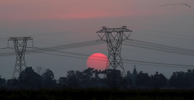 El sol se opne detras de unas torres de electricidad en Carletonville, al oeste de Johannesburgo. REUTERS/Siphiwe Sibeko