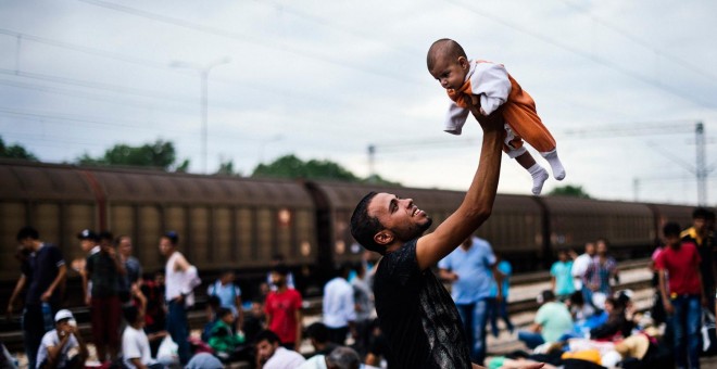 Un inmigrante levanta su bebé mientras espera un tren en dirección a la frontera con Serbia, en la estación de tren en Gevgelija, en la frontera de Macedonia y Grecia el 6 de agosto de 2015.- AFP PHOTO / DIMITAR DILKOFF