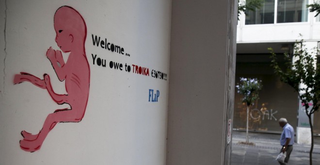 Una pintada en una calle de Atenas de un dibujo de un recién nacido con una frase que dice:  'Bienvenido ... le debes a la Troika 36.730 €'. REUTERS / Alkis Konstantinidis