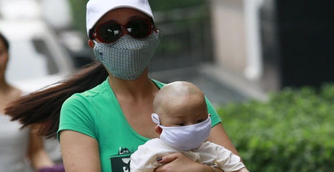 Una mujer con un bebé, ambos con máscaras, caminan por las calles de Tianjin. REUTERS