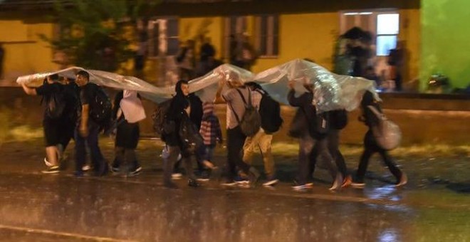Los migrantes se protegen de la lluvia con un plástico mientras caminan para coger el tren en dirección a la frontera con Serbia, después de recibir el permiso para cruzar en Macedonia en la estación de tren en Gevgelija.-EFE