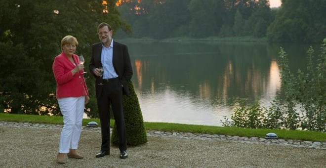 El presidente del gobierno español, Mariano Rajoy y la canciller alemana Angela Merkel por el entorno del lago de Schloss en el castillo de Meseberg (Alemanía). -EFE