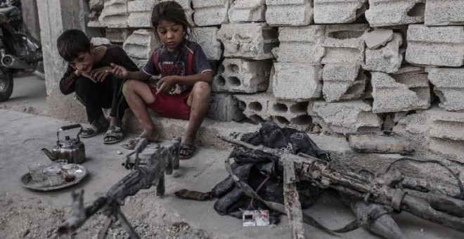 Dos niños permanecen en Kobani, Siria, junto a varias armas incautadas a combatientes del Estado Islámico. - AFP