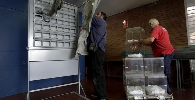 Dos operarios descargan varias urnas e instalan una cabina en un colegio electoral en Barcelona. EFE/Alberto Estévez