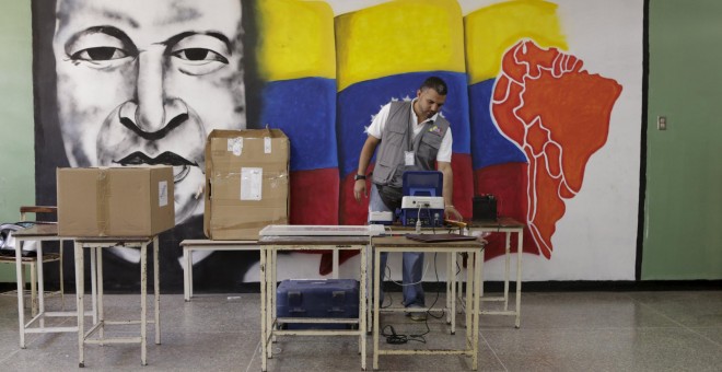 Un trabajador del Consejo Nacional Electoral perpara la máquina de votación junto a un mural con la imagen del expresidente venezolano Hugo Chavez, en un colegio de Caracas. REUTERS/Marco Bello