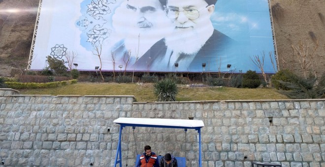 Dos jóvenes iraníes se sientan bajo una gran foto del fallecido líder de Irán, el ayatolá Jomeini, y el líder supremo de Irán, el ayatolá Ali Jamenei en un parque de Teherán, Irán. REUTERS