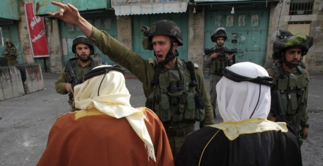 Un soldado israelí da órdenes a dos hombres palestinos durante una manifestación en Hebrón. - AFP