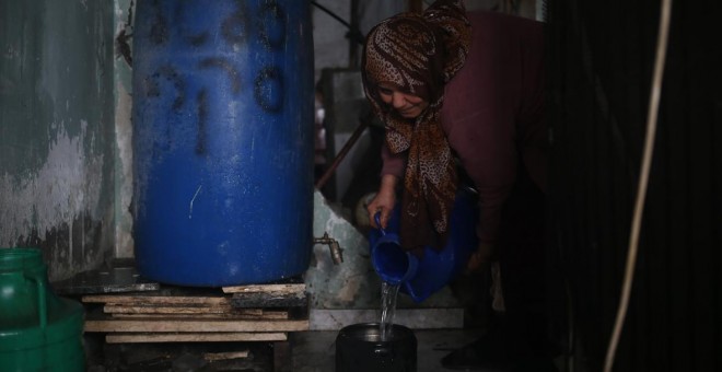 Etadal Abu Oda, una mujer palestina de 57 años de edad, toma agua de un tanque para limpiar los platos en su casa en Beit Hanoun, en el norte de la Franja de Gaza. Mohammed ABED / AFP