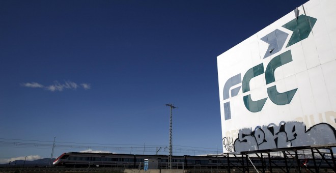 Un tren pasa cerca de un cartel de la empresa de construcción y servicios  FCC, cerca de la localidad madrileña de Tres Cantos. REUTERS/Susana Vera