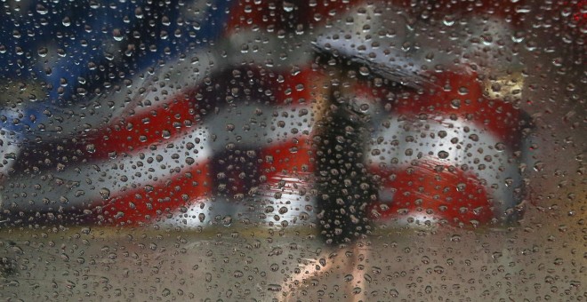 Una mujer anda bajo la lluvia junto a una bandera de EEUU pintada en un edificio en Manhattan. - REUTERS