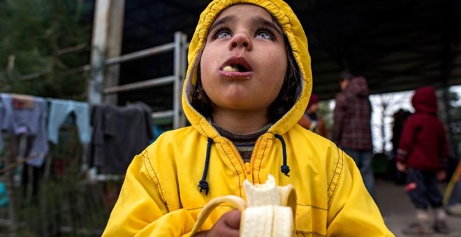 Una niña come un plátano en el campo de refugiados en Idomeni. EFE/ Georgi Licovski