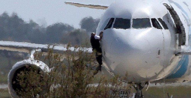 Dos hombres de los cuerpos de seguridad escalan por el avión egipcio secuestrado por un hombre en el aeropuerto de Chipre. REUTERS