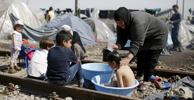 Una mujer baña a un niño encima de las vías del tren en el campo de refugiados de Idomeni . - REUTERS