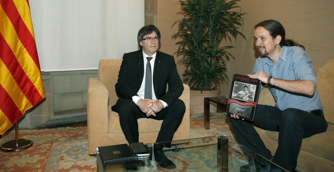 El presidente de la Generalitat, Carles Puigdemont, junto al líder de Podemos, Pablo Iglesias, quien sostiene el libro sobre Andreu Nin que le ha regalado. EFE/Andreu Dalmau