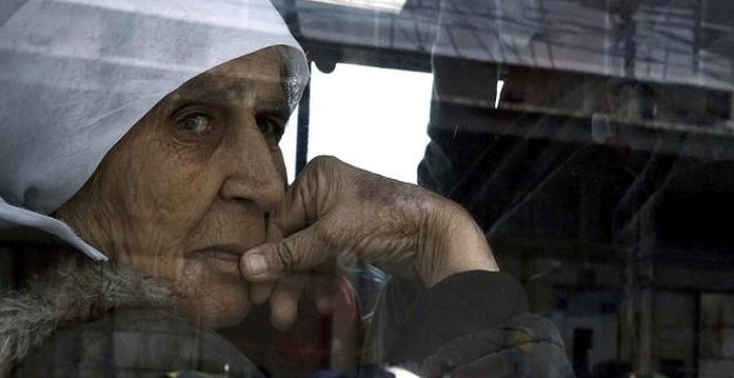 Una anciana mira por la ventana de un autobús que traslada a refugiados sirios e iraquíes a las nuevas instalaciones de acogida en el puerto de Skaramangas. EFE