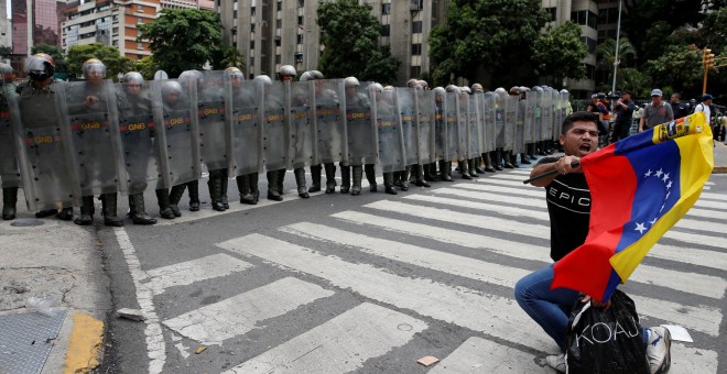 An opposition supporter carrying a Venezuelan flag kneels in front of National Guards during a rally to demand a referendum to remove President Nicolas Maduro in Caracas, Venezuela, May 18, 2016. REUTERS/Carlos Garcia Rawlins