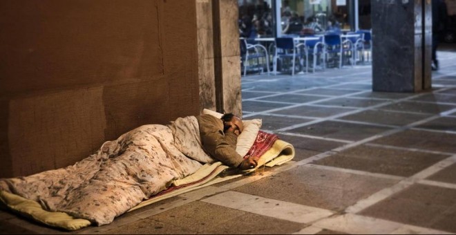 Un hombre sin techo duerme en la acera, junto a una cafetería. EFE