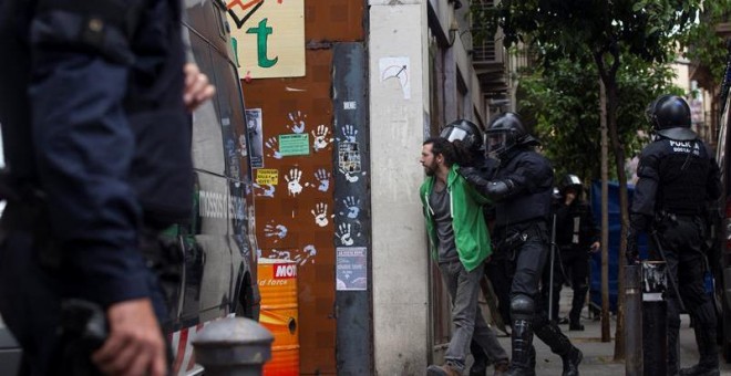 Mossos d'Esquadra custodian a uno de los okupas detenidos por volver a entrar en el edificio que llaman 'Banc Expropiat' del barrio barcelonés de Gràcia. EFE/Quique García