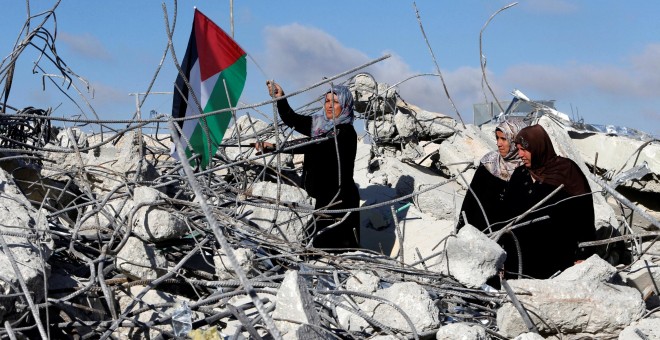 La madre de un supuesto asaltante palestino sostiene una bandera en el tejado de la casa familiar derruida por tropas israelíes. - REUTERS