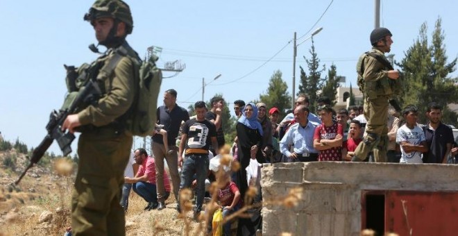 Palestinos esperan a poder cruzar un 'checkpoint' con soldados israelíes armados al sur de Hebrón. - AFP