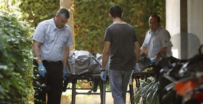 Miembros de los servicios funerarios trasladan el cadáver del hombre de 48 años localizado en un piso muy cerca de la entidad bancaria donde ha muerto a puñaladas su directora./ ANDREU DALMAU (EFE)