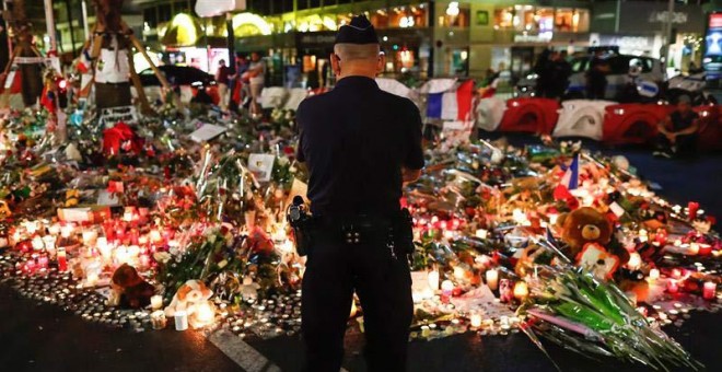 Un gendarme francés contempla las flores y las velas colocadas en el Paseo de los ingleses en Niza. / EFE