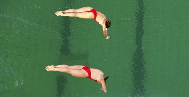 Dos nadadoras realizan un salto durante la competición desarrollada en la piscina con el agua de color verde.- REUTERS