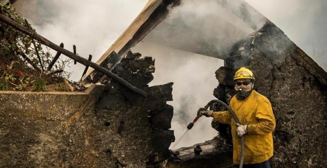 Un bombero refrescan los rescoldos tras incendiarse una casa en Fuchal, isla de Madeira (Portugal). Los tres fallecidos en los incendios que azotan Funchal, la capital del archipiélago luso de Madeira, son de la misma familia y hay un total de 300 heridos