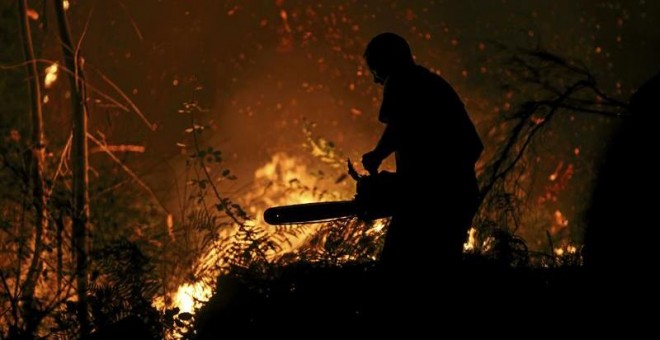 Un vecino intenta sofocar las llamas del incendio forestal de Arbo (Pontevedra), en el que se ha decretado la Situación 2 por la cercanía del fuego a núcleos de población. Las hectáreas de monte afectadas por los incendios forestales que se mantienen act
