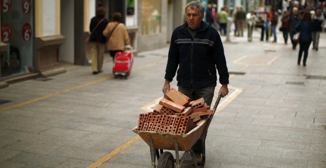 Un trabajador de la construcción traslada una carretilla con ladrillos por una calle de la localidad malagueña de Ronde. REUTERS/Jon Nazca