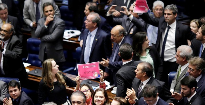 Varios senadores sujetan carteles contrarios al "golpe" contra Rousseff durante la votación en la Cámara. - REUTERS