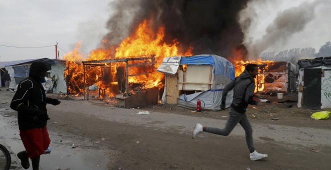 Varios inmigrantes se alejan del incendio en una de las tiendas de la Jungla. - REUTERS