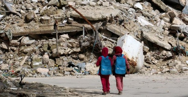 Dos niñas con mochilas donadas por UNICEF pasan junto a un edificio derruido en Alepo de camino a la escuela. Fotografía de marzo de 2015. - ZEIN AL-RIFAI (AFP)