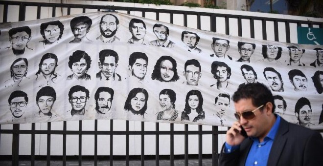 Un hombre pasa en Ciudad de Guatemala junto a un mural con rostros de desaparecidos durante el conflicto armado. - AFP