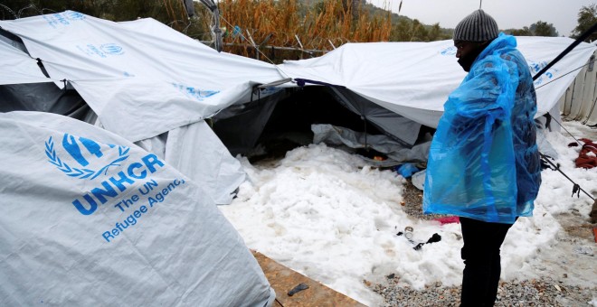 Un hombre trata de refugiarse del frío con un plástico en la isla griega de Lesbos. - REUTERS
