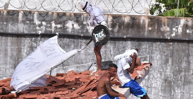 Varios presos, uno de ellos con un escudo con las iniciales del PCC, en un tejado de la prisión Alcacuz en Natal. - REUTERS