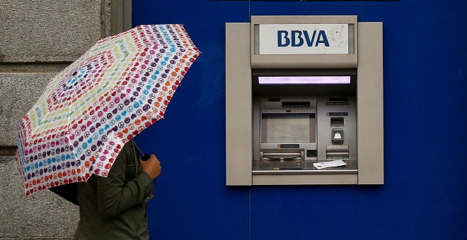 Una mujer con paraguas pasa junto a una oficina de BBVA en Madrid. REUTERS/Andrea Comas