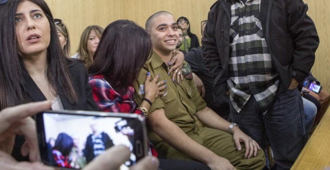El soldado israelí Elor Azaría (c), es abrazado por su madre antes de escuchar el veredicto de un Tribunal militar israelí en Tel Aviv que le ha declarado culpable de la muerte de un palestino, al que remató de un tiro en la cabeza mientras estaba en el s