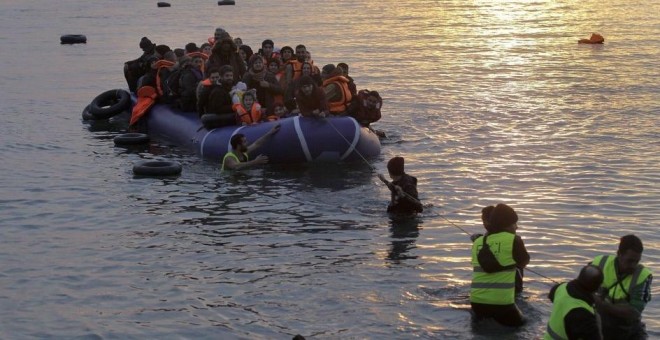 Voluntarios de una ONG ayudan a refugiados y migrantes que llegan en una lancha neumática a la costa de Mytilini, en la isla de Lesbos (Orestis Panagiotou / EFE)
