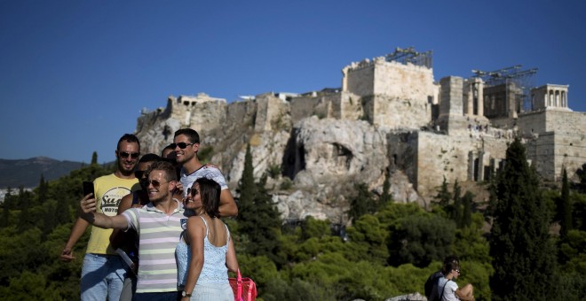 Unos turistas se toman un selfi desde la Colina de Ares, en Atenas, con la Acrópolis al fondo. REUTERS/Stoyan Nenov